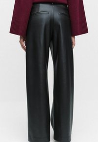 Mustat nahkaiset leveälahkeiset housut, joissa on sileä tekstuuri, varustettuna takataskuilla ja siistillä vyötäröllä, tyyliteltynä marooninvärisellä neuleella.