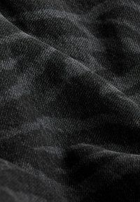 Tissu en denim noir avec une texture douce, présentant des variations subtiles de teinte et une finition lisse, légèrement mate.