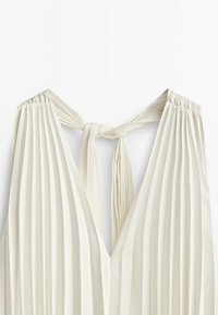 Haut en tissu plissé couleur crème avec un col en V profond et une fine bretelle nouée en nœud à l'arrière du cou.