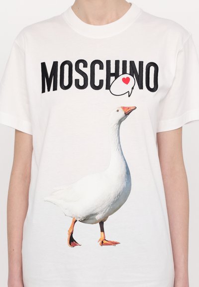 Balta medvilninė marškinėlių su grafika, vaizduojančia stovintį baltą žąsį ir užrašą "MOSCHINO" drąsiais juodais raidėmis viršuje.