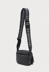 Μαύρη συνθετική τσάντα χιαστί με κλείσιμο φερμουάρ, διαθέτει πλεκτό ιμάντα με γκρι γεωμετρικά σχέδια και μπροστινή τσέπη.