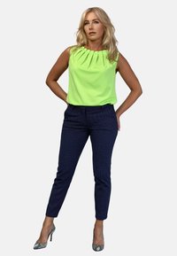 Neonowa zielona bezrękawnik z plisowanym dekoltem; granatowe spodnie w wzory; buty na obcasie z wężowej skóry. Prosty, nowoczesny design.