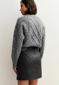 Grijze kabelgebreide trui met een textuurpatroon en geribde mouwen, gecombineerd met een fitted zwarte leren rok met een gladde afwerking en minimalistisch ontwerp.