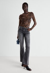 Langemouwen tijgerprint top, grijze flared jeans, zwarte open-toe hakken, met een kleine blauwe tas. Zachte textuur, aansluitend ontwerp.