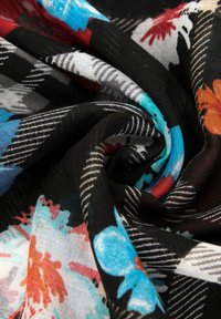 Tissu à motif floral coloré sur fond noir, présentant des tons de bleu, rouge et blanc, avec une texture légère et douce, drapé et froissé.