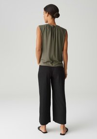 Olive green sleeveless top with gathered back detail, paired with loose black textured wide-leg pants and black flat sandals.