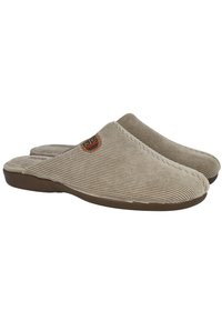 Zapatillas de casa de color beige, tipo slip-on, con textura de pana, punta redonda y suela de goma marrón claro. Incluyen un pequeño parche de logo en el costado.