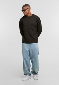 Black long-sleeve shirt, light blue baggy jeans, and white sneakers. The figure wears angular black sunglasses and has short, textured hair.