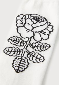 Vitt strumpa med svart broderad rosdesign, med detaljerade blad och kronblad med texturerade konturer.