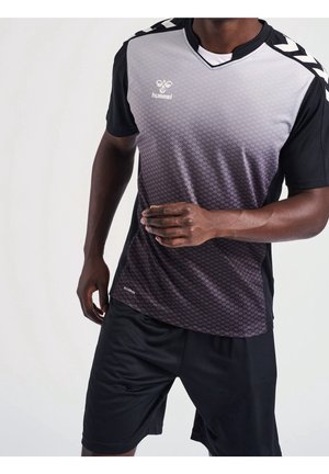 Man in zwart-grijs verloop sportshirt en zwarte shorts, staand met één arm gebogen en hand omhoog gehouden bij de borst.