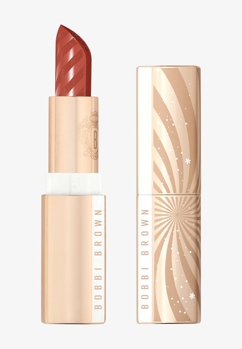 Lippenstift in einer goldenen Tube mit eingraviertem Logo. Die Farbe ist ein warmes rötlich-braun mit subtilen Streifen auf der Kappe. Dekoratives, spiralförmiges Muster auf der Verpackung.