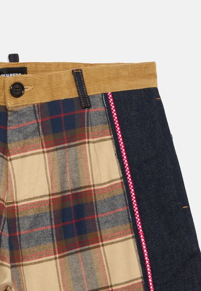 Gros plan d’un pantalon avec une ceinture en velours côtelé marron, un bouton et un tissu à carreaux d’un côté et un tissu en denim foncé de l’autre avec une couture rouge.