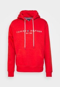 Sudadera roja hecha de una mezcla de algodón. Presenta un bolsillo tipo canguro en el frente, capucha con cordón y un logo bordado en blanco que dice "EST. 1985."