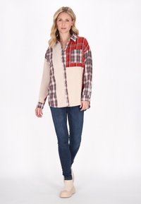 Camicia a maniche lunghe con un design a quadri nei toni di rosso, grigio e beige, dotata di una tasca sul petto. Abbinata a jeans skinny blu scuro.