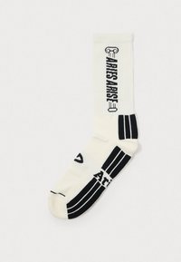 White crew sock with black graphic designs, including "ARTISAN" text, and three black stripes at the ankle. Ribbed texture.
