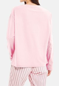 Ljusrosa långärmad skjorta med avslappnad passform, med rundad halsringning och sytt fåll, som kombineras med randiga pyjamabyxor.