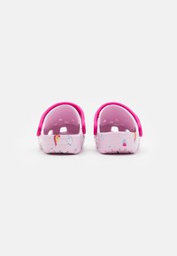 Różowe klapki dla dzieci z wzorami tęcz i chmur, różowe regulowane paski na piętach, pokazane z tyłu na białym tle.