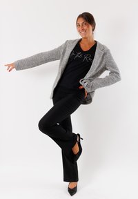 Blazer grigio testurizzato su una t-shirt nera con un design a scritta, abbinato a pantaloni neri attillati e scarpe con tacco nere.