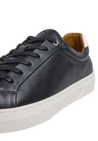 Svarta lädersneakers med rund tå, vit gummisula och texturerad tunga. Har svarta snören och en präglad logotyp på sidan.