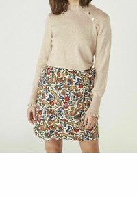 Ljusrosa stickad tröja med ribbad textur och volangärmar, kombinerad med en krämfärgad kjol med ett färgglatt blommigt paisleymönster.