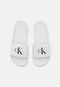 Infradito bianchi con una fascia in tessuto che presenta il logo "CK" nero e la scritta dorata "Calvin Klein Jeans". Soletta leggermente testurizzata, suola piatta.