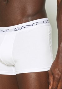 Valged puuvillased bokserid pehme elastse vöökoha ja tumesinise "GANT" logo kuriga. Sile tekstuur, lähedalt liibuv disain ja keskmise reie pikkus.