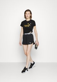 Black athletic outfit consisting of a fitted T-shirt with gold logo and black shorts with a white waistband; paired with black and white sneakers.