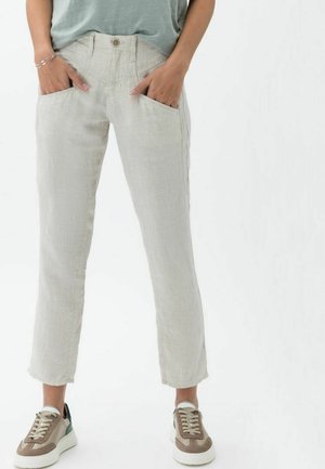 Pantalons en lin beige clair avec une coupe droite, dotés de poches avant et d'une fermeture à bouton. Associés à des baskets beige et vert.