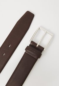 Curea din piele maro cu o cataramă argintie, având numele brandului "GANT" gravat pe piele aproape de cataramă.