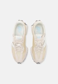 Paire de baskets beiges et blanches avec lacets et semelle à motif, vues de dessus sur un fond clair.