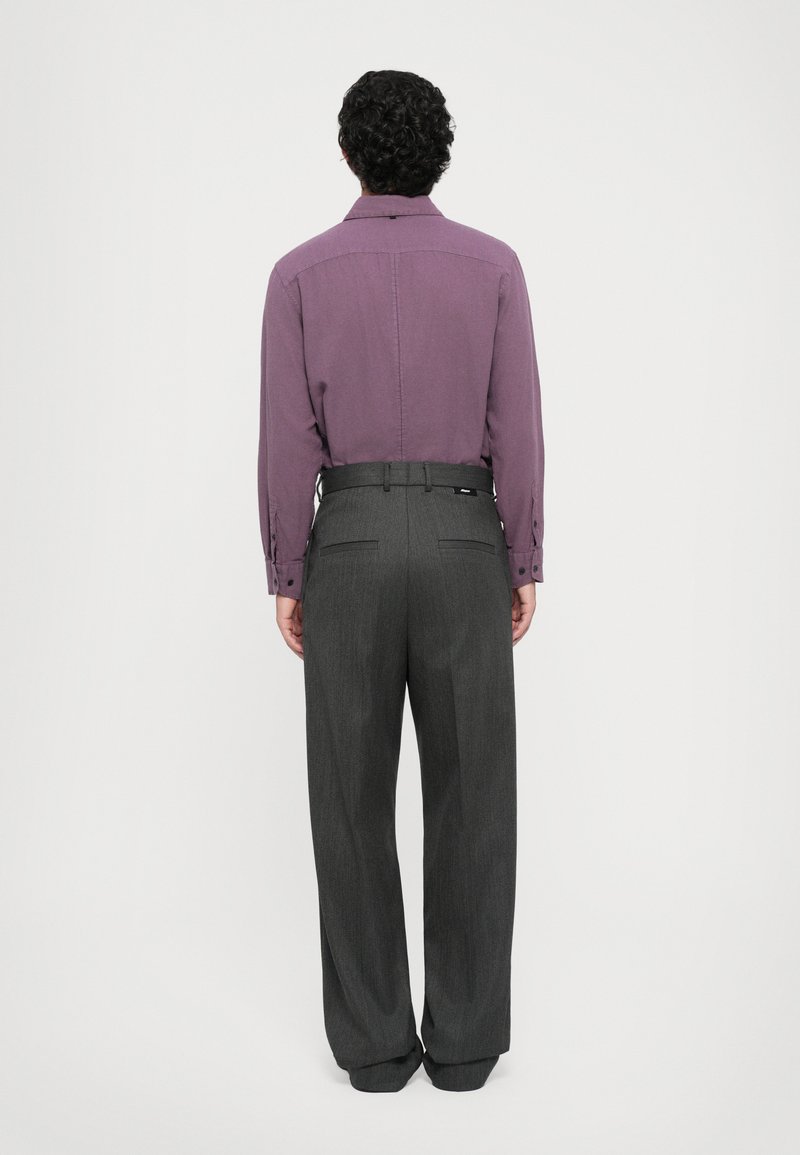 Chemise à manches longues violette avec des poignets boutonnés, associée à un pantalon gris taille haute. Le pantalon présente une coupe droite et des poches arrière.