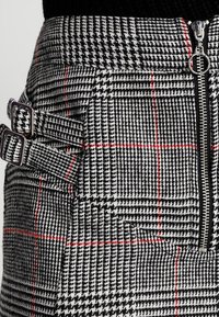 Svart och vit rutigt kjol med röda detaljer, med en sidodragkedja och två justerbara spännen i midjan.