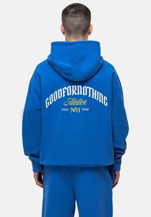 Sweat à capuche en coton bleu avec une coupe loose. Présente un grand texte blanc et jaune au dos. Le texte inclut "GOODFORNOTHING" et "Atelier."