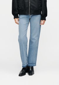 Φαρδιά τζιν παντελόνια σε ανοικτό γαλάζιο με ξέφτια στα τελειώματα, συνδυασμένα με μαύρα μποτάκια αστραγάλου  και μαύρο μπουφάν bomber. Το ύφασμα φαίνεται τζιν με ελαφριά υφή.