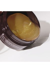 Récipient marron foncé avec un couvercle transparent, contenant un gel doré semi-translucide à l'intérieur. Le gel a une texture brillante et scintillante.