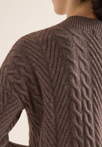 Brązowy sweter w splot kablowy z teksturowanym wzorem w zygzak i ribbanym okrągłym dekoltem, wykonany z miękkiego, ciepłego materiału.