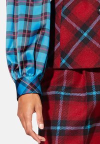 Blauwe en zwarte geruite mouw met een geplooid ontwerp, gecombineerd met een rode en zwarte geruite kledingstuk. Opvallend contrast in kleuren en patronen.