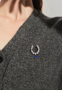 Hopeakoru, jossa on U-muotoilu, kirkkailla kivillä ja sinisellä kivityöllä, tummanharmaalla teksturoidulla kankaalla.