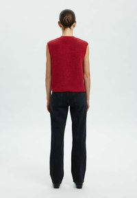 Top sans manches en tricot rouge avec une finition texturée, associé à un jean noir taille haute. Silhouette simple et ajustée à la taille.