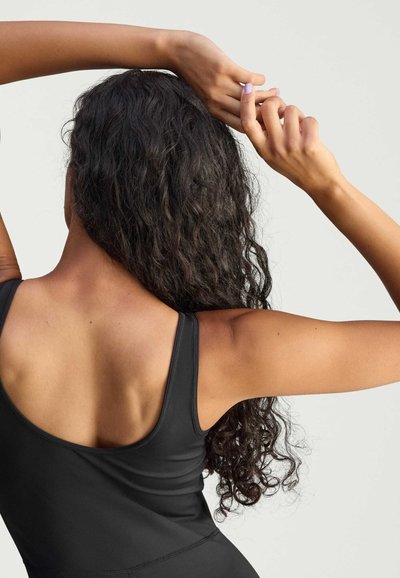 Black athletic top with wide straps, smooth texture, and a fitted design, worn by a person with curly hair, showing their back and arms.