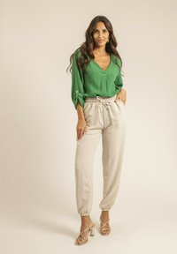 Blouse verte texturée avec un décolleté en V et des manches retroussées, associée à un pantalon jogger couleur crème avec une taille élastique, et des sandales dorées.