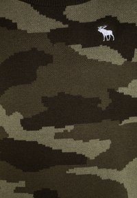 Sweter w kolorze zielonym i oliwkowym z dzianiny w kamuflaż. Posiada małe, białe, haftowane logo z łosiem na górze z lewej strony.