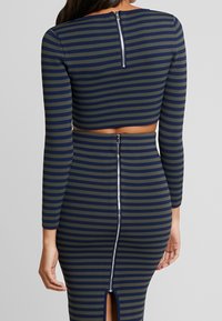 Striped two-piece outfit featuring a cropped top and fitted skirt, in navy blue and olive green. Back zip closure and high slit detail.
