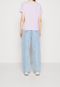 Lyslilla kortærmet t-shirt med afslappet pasform, kombineret med højtaljede lyseblå vidde jeans og hvide sneakers.