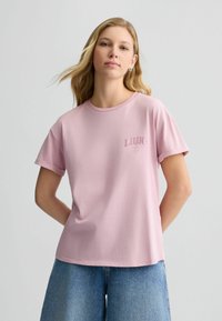 Tricou din bumbac roz, cu decolteu rotund și mâneci scurte, având un mic logo brodat pe piept și o croială lejeră.