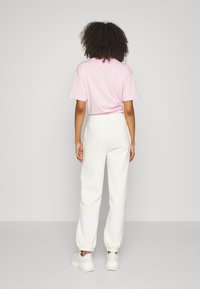 Rosa bomull T-skjorte med korte ermer, sammen med kremfargede joggebukser. Buksene har elastisk liv og samlet ankel. Hvite sneakers.