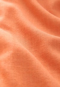 Korallinvärinen kangas, jossa on teksturoitu, kudottu pinta, sileitä taitoksia ja hienovaraisia sävy- ja valovaihteluita.