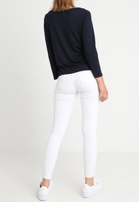 Langärmliges navy Oberteil in Kombination mit figurbetonten weißen Jeans und weißen Sneakern, die eine glatte Textur und ein schlichtes Design präsentieren.