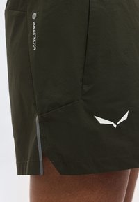 Σκούρα πράσινα σορτς με άσπρο κείμενο "DURASTRETCH" και αφηρημένο λευκό λογότυπο, με πλαϊνή σχισμή και λεπτομέρεια με αντανακλαστική ταινία.