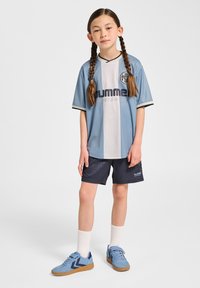 Sportkläder bestående av en ljusblå och vit kortärmad tröja med en logga, kombinerad med marinblå shorts och blå sneakers.